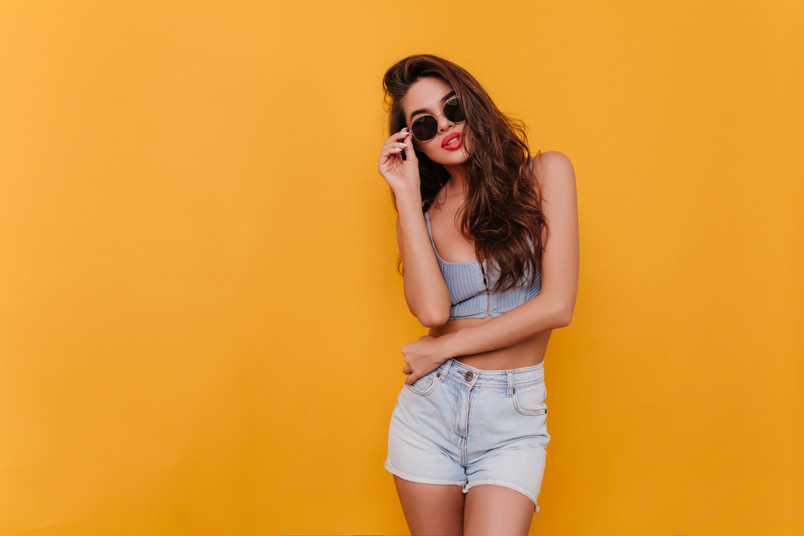 Amazing slim lady in casual outfit standing in confident pose on yellow background. Indoor photo of lovely girl with long dark hair sensually posing.